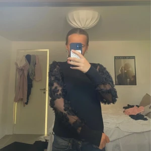 Svart topp med meshärmar från JDY - Säljer en svart topp från JDY i storlek S med unika meshärmar dekorerade med 3D-blommor. Tröjan har lång ärm och en normal passform. Materialet är mjukt och stretchigt med detaljer i mesh och blommor. Använd endast 2-3 ggr och är perfekt för fest!