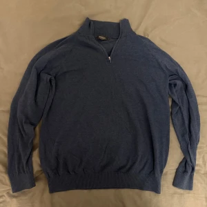 Blå halvzip tröja från Dressmann - Superskön blå tröja från Dressmann i Supima-bomull. Tröjan har en ribbad hög krage och dragkedja framtill (half zip). Långärmad modell med ribbade muddar och nederkant. Perfekt för lager-på-lager och chill stil. Priset inte hugget i pris vid snabbaffär!