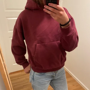 Vinröd hoodie med magficka - Säljer en vinröd hoodie med stor magficka och huva. Tröjan har ribbade muddar vid ärmslut och nederkant. Säljer pga för liten.