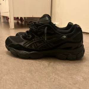 Svarta Asics sneakers strl 43.5 - Säljer ett par helsvarta Asics sneakers med mesh och syntetdetaljer. Skorna har snörning, rund tå och en rejäl platt sula som ger grym komfort. Perfekt för dig som gillar sportig stil och vill ha ett par schyssta sneakers till vardags. Kan diskutera pris 