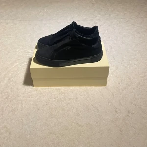  Axel Arigato skor - Snygga svarta sneakers från Axel Arigato med minimalistisk design och diskret logga på sidan. Skorna har en platt sula och är tillverkade i mocka för en lyxig känsla. Perfekt för dig som gillar stilrena och moderna skor.