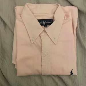 Rosa Ralph Lauren skjorta  - Säljer denna stilrena och snygga rosa Ralph Lauren-skjorta i helt nyskick! Perfekt för allt från vardaglig stil till finare tillfällen. Den ikoniska broderade loggan på bröstet ger skjortan en exklusiv och tidlös look.  ✅ Storlek: M 🌸 Färg: Ljusrosa ✨ Skick: Helt nyskick 👔 Detaljer: Klassisk button-down krage & långärmad