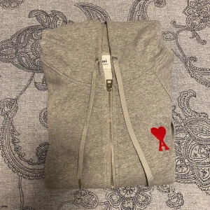 Grå Ami de Coeur zip-up hoodie - Säljer en snygg grå hoodie från Ami med dragkedja och huva. Fint broderat hjärta med bokstaven A på bröstet. Hyfsat ny och har används få gånger, så 10/10 kvalité. 