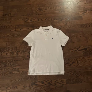 Vit pikétröja från Morris Stockholm - Klassisk vit pikétröja från Morris Stockholm i storlek S. Tröjan har korta ärmar, krage och knäppning framtill samt en liten broderad logga på bröstet. Tillverkad i mjuk bomull som känns skön mot huden. Perfekt för en clean och stilren look.