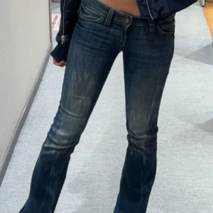 Cheap Monday jeans - Snygga mörkblå jeans från weekday med bootcut passform och coola slitningar framtill. De har en grön patch med tryck på bakfickan och klassisk femficksdesign. Jeansen har låg midja och är gjorda i jeansmaterial med dragkedja och knapp framtill. Storlek W27 L32