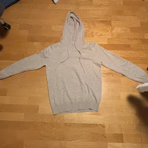 Beige hoodie från Bvaldi med brodyr - Säljer en stilren beige hoodie från Bvaldi med broderad logga på bröstet. Tröjan har huva med snörning och är långärmad. Perfekt för dig som gillar en enkel och clean look. Materialet känns mjukt och skönt mot huden.