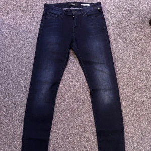 Replay Luzien mörkblå jeans - Mörkblå jeans från Replay, modell Luzien med hög midja. Jeansen har klassisk femficksdesign, smal passform och är tillverkade i stretchigt denim för extra komfort. Perfekt för dig som gillar en stilren look.