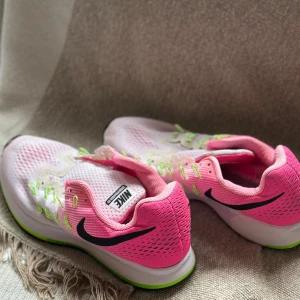 Nike Zoom Pegaus  sneakers rosa och vit - Nike Zoom sneakers i en fräsch mix av rosa och vit med svarta detaljer och limegröna snören. Ovandelen är ventilerande mesh och sulan har grymt grepp med svart och limegrön kant. Perfekt för dig som gillar sportig stil och vill sticka ut med färg.