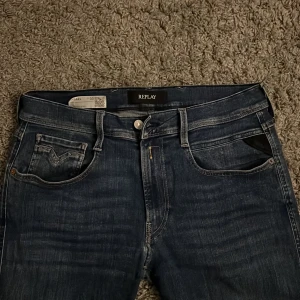 Replay Anbass Hyperflex jeans blå - Snygga Replay Anbass Hyperflex jeans i mörkblå tvätt med klassiska fem fickor och svarta Replay-lappen bak. Slimmad passform och stretchigt material för extra komfort. Perfekt för dig som gillar stilrena och moderna jeans.