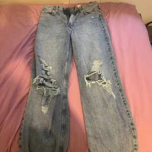 Loose fit ripped jeans från &Denim - Säljer ett par ljusblå loose fit jeans från &Denim i storlek 36. Byxorna har high waist, raka ben och stora slitningar med fransiga detaljer på båda benen. Perfekt för dig som gillar en avslappnad och trendig look.