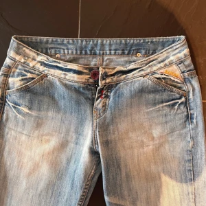 Snygga Jeans från replay - Snygga ljusblå jeans från Replay med slitna detaljer och raka ben. Jeansen har coolt rött broderi på bakfickorna och klassisk femficksdesign. De är tillverkade i mjukt denim och har en normal passform med låg midja.