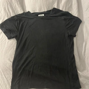 Svart t-shirt från Weekday XS - En klassisk svart t-shirt från Weekday i storlek XS. T-shirten har rund halsringning och korta ärmar, perfekt för en clean och enkel look. Tillverkad i mjuk bomull som känns skön mot huden.
