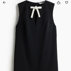 Svart kort klänning med pärlrosett - Ordinarie pris 499kr, använd en gång. Supersnygg svart ärmlös klänning från H&M Edition i kort modell. Framtill finns en dekorativ vit rosett med pärlor vid halsen som ger en extra touch. Klänningen har en rak passform och är tillverkad i ett mjukt, slätt material. Perfekt för dig som gillar stilrena detaljer.