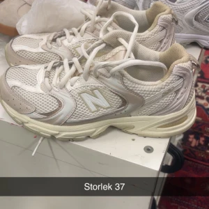 Vita New Balance sneakers strl 37 - Säljer ett par snygga New Balance sneakers i vitt och beige med mesh och syntetdetaljer. Skorna har klassisk snörning och en chunky sula som ger skön komfort. Perfekta för dig som gillar sportig och trendig stil.