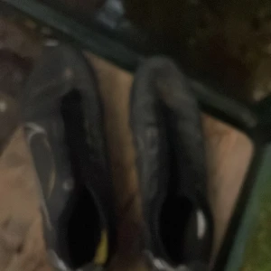 Svarta Nike fotbollsskor med guldiga detaljer - Säljer ett par svarta Nike fotbollsskor med snygga guldiga detaljer och stor vit swoosh på sidan. Skorna har låg profil, platt sula med dobbar och är tillverkade i syntetmaterial. Perfekta för dig som vill sticka ut på planen med stilren design.