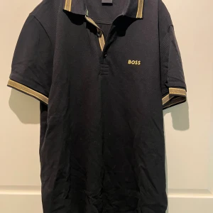 Svart Boss pikéskjorta med gulddetaljer - Knappt använd så i nyskick.