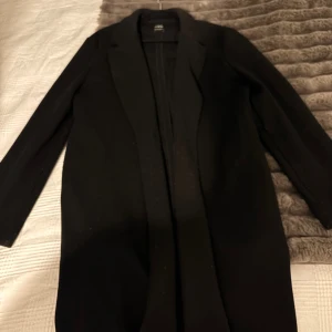 Svart kappa från Zara - Säljer en stilren svart kappa från Zara med klassisk krage och lång passform. Jackan har två öppna fickor. Den är knappt använd och i mycket bra skick. 