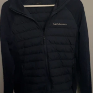 Mörkblå cardigan från Peak Performance - Säljer en mörkblå jacka från Peak Performance med dragkedja framtill. Jackan har en quiltad design och långa ärmar, perfekt för kyligare dagar. Den är stilren och funktionell, idealisk för både vardag och utomhusaktiviteter.