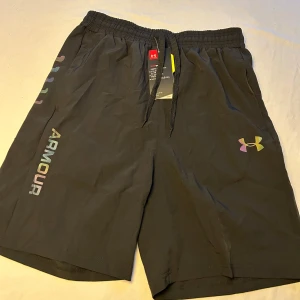 Svarta träningsshorts  - Svarta träningsshorts med elastisk midja och snörning. Logga och text i regnbågsfärger på benet ger en snygg touch. Lätta och luftiga, perfekta för gymmet eller löprundan.