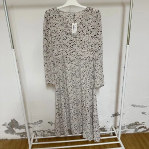 Blommig långklänning från Indiska - Snygg långklänning från Indiska med svartvitt svart vitt mönster. Klänningen har rund hals, långa ärmar och knappar framtill. Tillverkad i mjuk viscose som faller fint och ger en skön känsla. Perfekt för dig som gillar stilrena och feminina detaljer. Prislappen kvar och helt oaanvänd.