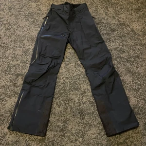 Peak Performance skidbyxor skalbyxor - Säljer ett par svarta byxor med flera praktiska dragkedjor och fickor. Byxorna har en loose passform och är perfekta för utomhusaktiviteter. De har förstärkta partier vid knäna och bensluten för extra hållbarhet.