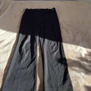 Svarta kostymbyxor från Sinéquanone - Stilrena svarta kostymbyxor från Sinéquanone med klassisk rak passform och vida ben. Byxorna har bälteshällor, knappstängning i midjan och är tillverkade i ett mjukt tyg som ger en dressad look. Perfekta för dig som gillar en clean och tidlös stil.