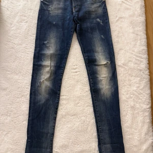 Mörkblå skinny jeans med slitningar - Snygga mörkblå jeans mid waist med skinny fit och slitna detaljer på benen. Jeansen har klassisk femficksdesign och ljusare partier framtill och baktill för en cool, använd look. Perfekta för dig som gillar en smal siluett och streetkänsla.