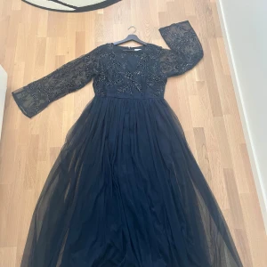 Marinblå långklänning från Boohoo - Säljer en marinblå långklänning från Boohoo Occasion med transparenta långärmar och vackra broderade blommor med pärldetaljer upptill. Kjolen är i flera lager tunn mesh som ger ett flowy intryck. Perfekt för dig som vill sticka ut med elegans.