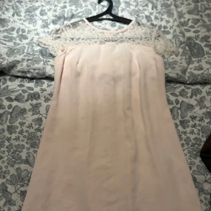 Ljusrosa spetsklänning från Stockh LM - Superfin ljusrosa kortklänning från Stockh LM med spets upptill och ärmlös design. Klänningen har rund halsringning och vackra spetsdetaljer över axlar och rygg. Perfekt för dig som gillar romantisk och feminin stil.