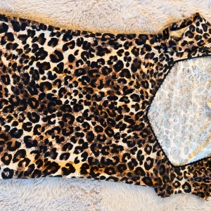 Leopardmönstrad klänning från Nelly - Snygg kort klänning från Nelly i leopardmönster med v-ringad hals och svarta spetsdetaljer längs kanten. Klänningen har en figurnära passform och är perfekt för dig som vill sticka ut. Färgerna går i beige, brun och svart.