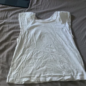 Vit ärmlös topp med spets från H&M - Säljer en vit ärmlös topp från H&M i storlek S. Toppen har broderade spetsdetaljer på axlarna och en rund halsringning. Perfekt för sommarens varma dagar och enkel att matcha med jeans eller kjol.