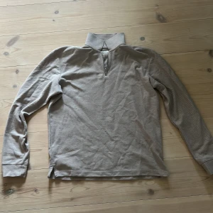 Beige långärmad pikétröja med zip - Säljer en beige långärmad pikétröja från Oscar Jacobson med klassisk krage och half zip framtill. Tröjan är i mjuk bomull och har en stilren, enkel look som passar perfekt till lager-på-lager. Snygg till både jeans och chinos.
