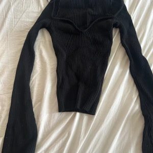 Svart ribbad långärmad topp - Säljer en svart ribbad långärmad topp från hm. Toppen har en snygg v-ringad skärning och är figurnära med offshoulder-design. Perfekt för dig som gillar en stilren och trendig look.