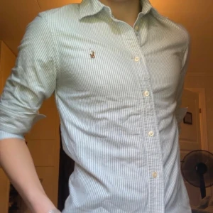 Randig skjorta från Ralph Lauren - Snygg skjorta från Ralph Lauren i vit och blå med tunna ränder. Klassisk krage, knäppning framtill och broderad logga på bröstet. Skjortan är långärmad och har en custom fit-passform. Perfekt för dig som gillar stilrena och tidlösa plagg. Passar för xs, pris kan såklart diskuteras och skriv vid eventuella frågor / prisförslag 