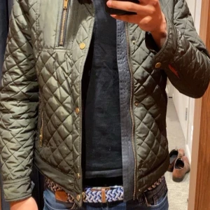 Olivgrön quiltad jacka Saki - Hej! Jag säljer nu min olivgröna jacka från Saki. Jackan har lång ärm, ståkrage med ribbade detaljer och orangefärgat innerfoder. Perfekt för dig som vill ha en stilren och modern look.