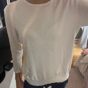 Vit prickig tröja från KappAhl - Superfin vit tröja från KappAhl med diskreta prickar i strukturen. Tröjan har rund halsringning och långa ärmar, perfekt för dig som gillar en clean och söt look. Mjuk och skön, passar till allt!
