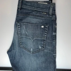 Diesel jeans - Snygga blåa jeans från Diesel med slitna detaljer och diskret tvättade partier. Klassisk femficksmodell med silverfärgade nitar och knappstängning. Jeansen har låg midja och är tillverkade i stretchig denim.