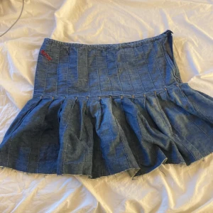 Jeanskjol med volang från Replay - Säljer en blå jeanskjol från Replay med volang nertill och broderad röd logga upptill. Kjolen har en kort modell och markerade sömmar som ger en cool look. Perfekt för dig som gillar denim och vill sticka ut lite extra.