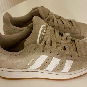 Beige Adidas Campus sneakers mocka - Säljer ett par beige Adidas Campus sneakers i mocka med klassiska vita ränder på sidorna och gummisula. Skorna har snörning, rund tå och Adidas logga på plösen. 