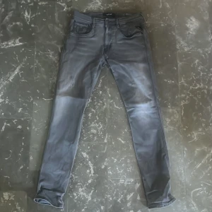 Grå anbass jeans från Replay - Snygga grå jeans från Replay med skinny passform. Klassisk slim fit med svarta detaljer och broderade bakfickor. Jeansen har dragkedjegylf och är tillverkade i stretchigt material för en bekväm känsla. Småhål precis vid sömmarna och är mycket lättsydda och därav priset, vid frågor eller funderingar är det bara att höra av sig 