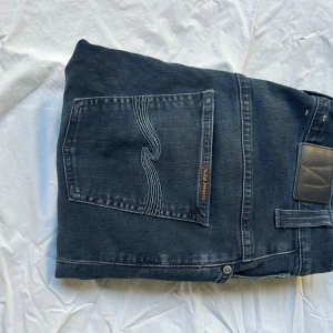 Nudie Jeans Thin Finn svarta jeans - Säljer ett par svarta Nudie Jeans Thin Finn i modellen. Jeansen har klassisk femficksdesign, dragkedja och snygga kontrastsömmar på bakfickan. Tillverkade i 98% ekologisk bomull och 2% elastan för en bekväm passform.