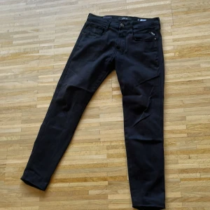 Svarta Replay Anbass Hyperflex jeans - Svarta Replay Anbass Hyperflex jeans med klassisk femficksdesign och snygga detaljer som metall-logga på bakfickan. Stretchigt material för extra komfort och smal passform. Perfekta för dig som gillar stilrena och moderna jeans. Storlek 31/32