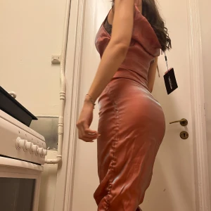 Rosa Klänning med Snörning - PRISLAPP KVAR! Säljer en glansig rosa långklänning med axelband med snörning. Klänningen har en rynkad effekt vid sidorna & en figurnära passform. 💖 Fraktar/Möts upp i Solna. Kolla min profil för mer kläder <3 Paketpris gäller! 