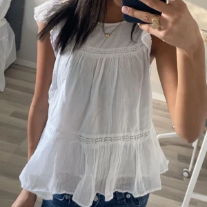 Vit blus med volang från Gina Tricot - Supersöt vit blus från Gina Tricot Young med volangkant nertill och fina spetsdetaljer. Blusen är ärmlös med lätt rynkade axlar och har en luftig, flowy passform💕💕