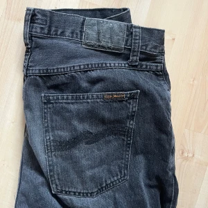 Nudie Jeans Rad Rufus Vintage Black 33/32 - Säljer ett par svarta Nudie Jeans Rad Rufus i modellen Vintage Black. Jeansen är raka i passformen, har klassisk femficksdesign och är tillverkade i 100% bomull. Snyggt broderad bakficka och diskret logga på baklappen.