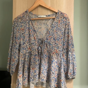 Mönstrad blus från Pull&Bear - Supersöt blus från Pull&Bear med paisleymönster i blått, beige och rost. Blusen har v-ringning med snörning framtill, volang nertill och trekvartsärmar med resår. Tunt och luftigt material!