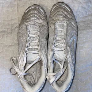 Nike Air Max 720 silver sneakers - Nike Air Max 720 sneakers i silver med vågig mesh-överdel och stora genomskinliga sulor. Snygg futuristisk design med vita och grå detaljer, snörning och rund tå. Perfekta för dig som gillar streetstyle och vill sticka ut med en unik look. Innersula saknas.