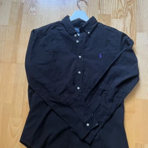 Svart skjorta från Polo Ralph Lauren - Svart skjorta från Polo Ralph Lauren i slim fit med klassisk krage och knappar framtill. HELT NY 