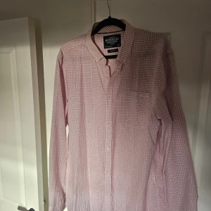 Rutig rosa skjorta från Bondelid - Säljer en klassisk rutig skjorta från Bondelid i rosa och vitt. Skjortan har lång ärm, knappar framtill och en bröstficka. Perfekt passform med skräddad siluett och mjukt bomullsmaterial. Snygg till jeans eller chinos.