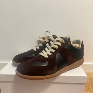 Bruna sneakers från Maison Margiela  storlek 43 - Snygga bruna svarta Maison margiela sneakers i storlek 43 som är använda 1 gång. Kvitto finns, låda dustbag kommer med också. Haft de ungefär ett halvt år. Skriv vid någon fundering för dig som gillar stilrena och tidlösa sneakers. Hör gärna av dig vid någon fundering 